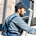 A worker stands on a ladder to assess a rooftop. 
